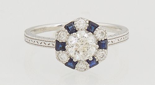 Lady's Platinum Dinner Ring, with a central .51 ct. round diamond atop a border of round diamonds, alternating with baguette sapphires, on a thin reli