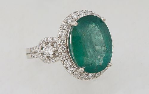 Lady's Platinum Dinner Ring, with an oval 8.13 carat emerald atop a border of small round diamonds, flanked by diamond mounted pierced lugs and diamon