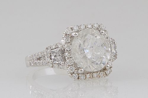 Lady's 18K White Gold Dinner Ring, with a 5.03 ct. round diamond atop a border of small round diamonds, flanked by baguette diamond lugs within diamon