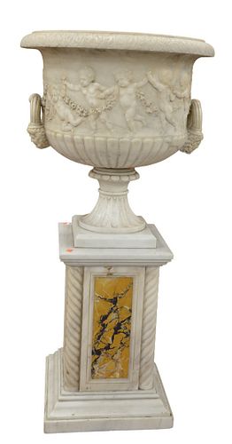 Carrera Marble Neoclassical Urn On Pedestal, having carved edge over putti, flowers, and two mask handles on pedestal with spiral columns and specimen