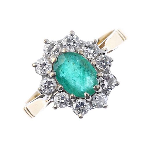 A 9ct gold emerald and diamond cluster ring. The oval-shape emerald, within a brilliant-cut diamond
