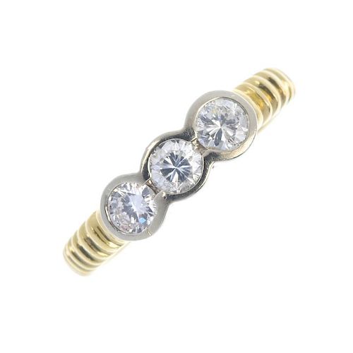 An 18ct gold diamond three-stone ring. The brilliant-cut diamond collets, to the ridged shoulders an