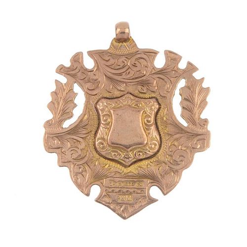 An early 20th century 9ct gold medallion. The raised shield-shape centre, within a scrolling surmoun