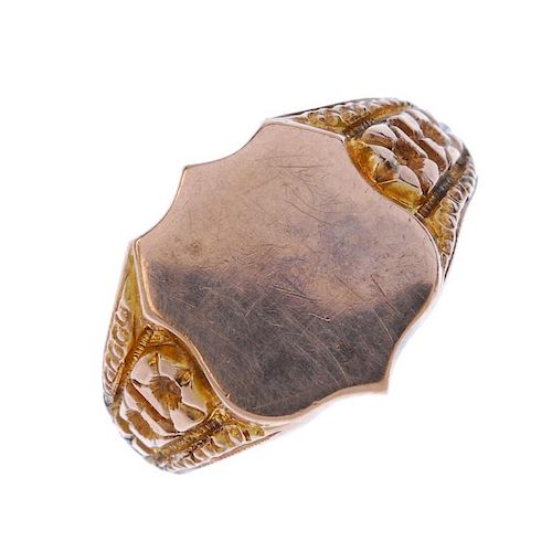 An early 20th century 9ct gold signet ring. The shield-shape panel, to the floral sides and plain ha