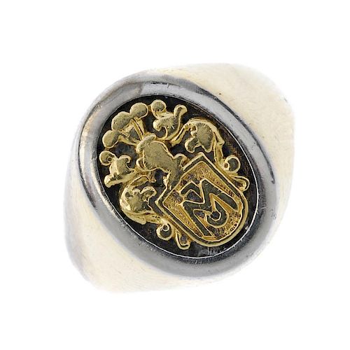 A signet ring. Of bi-colour design, the oval-shape panel, depicting a stylised armorial, to the plai