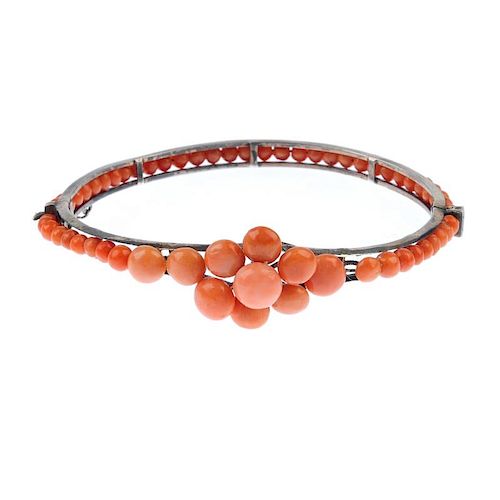 A coral bangle. Designed as a tapered front half bangle set with circular coral cabochons to the gra