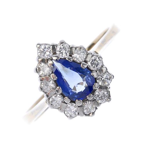 An 18ct gold sapphire diamond cluster ring. The pear-shape sapphire, within a brilliant-cut diamond