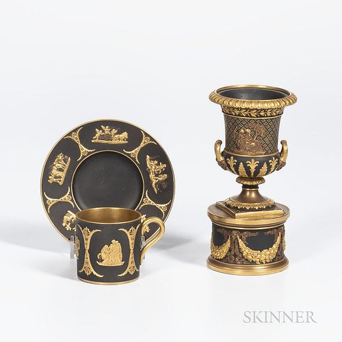 Two Wedgwood Gilded Black Basalt Items, England, c. 1885, a coffee can and saucer with classical figures within scrolled foliate frames, saucer dia. 4