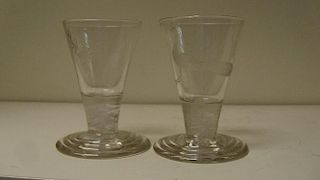 A pair of early 19th century firing glasses, the conical bowls engraved with stags' heads and peacoc