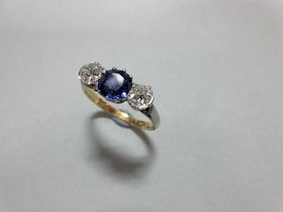 A three stone sapphire and diamond ring, claw set with a round cut royal blue sapphire between old c