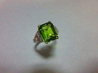 A 1930s style peridot and diamond ring, the emerald cut peridot measuring 10.6 x 8.7mm, four claw se