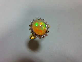 An opal and diamond cluster ring, the oval cabochon opal, displaying vivid predominently green and o