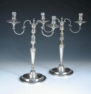 A pair of continental metalwares candelabra, unmarked, each raised from a circular foot with chased