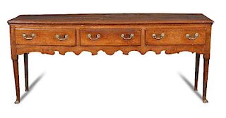 A George III oak dresser base, fitted three drawers with brass handles, shaped fret carved apron on