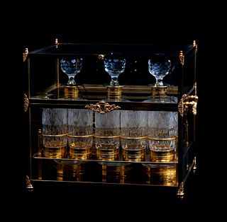 Caja licorera. Origen europeo, SXX. Elaborada en metal dorado y vidrio biselado. Con 3 licoreras y 10 vasos de cristal al interior.