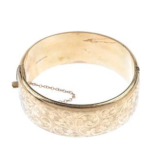 A mid 20th century 9ct gold hinged bangle. The hollow bangle, with foliate and scroll motif, to the