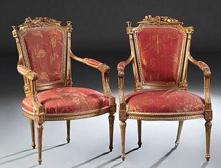 Pair of French Carved Giltwood Louis XVI Style Fauteuils, early 20th c., the musical instrument carved crest, flanked by trumpet form finials over a c