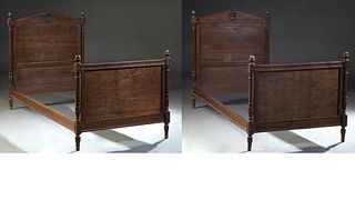 Pair of French Empire Carved Walnut Beds, 19th c., the peaked headboard with a central floral carving and acorn finials, to wood rails and a floral ca