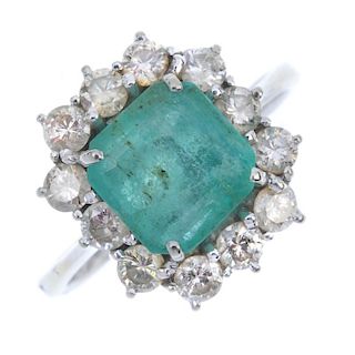 An emerald and diamond cluster ring. The square-shape emerald, within a brilliant-cut diamond surrou