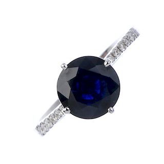 A sapphire and diamond ring. The circular-shape sapphire, to the brilliant-cut diamond line sides an