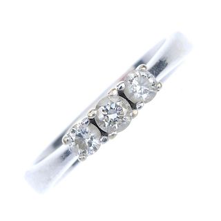 A diamond three-stone ring. The graduated diamond line, to the tapered shoulders and plain band. Est