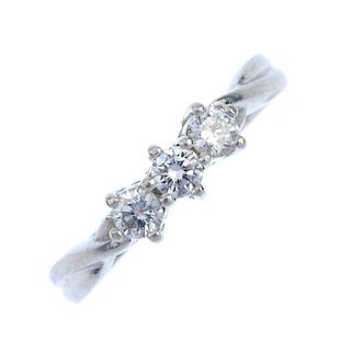 A platinum diamond three-stone ring. The brilliant-cut diamond line, to the crossover shoulders and