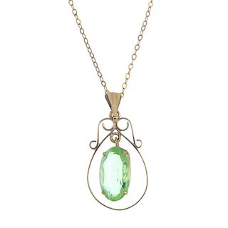 A 9ct gold paste single-stone pendant. The oval-shape green paste drop, suspended within a scroll su