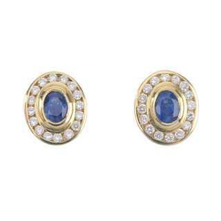 A pair of sapphire and diamond ear studs. Each designed as an oval-shape sapphire, within a brillian