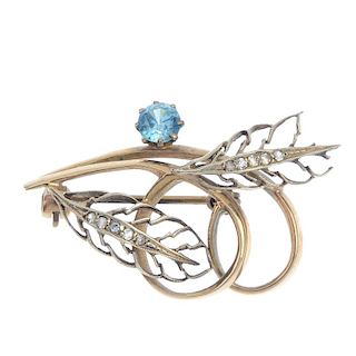 A 9ct gold zircon brooch. The scrolling fronds, with paste openwork foliate and circular-shape blue