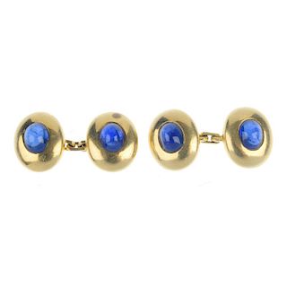 A pair of sapphire cufflinks. Each designed as an oval sapphire cabochon, within a wide surround, to