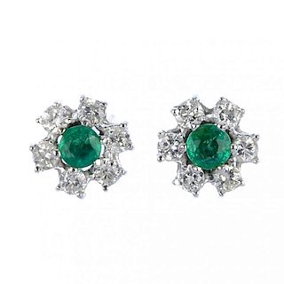 A pair of emerald and diamond ear studs. Each designed as a circular-shape emerald, within a brillia