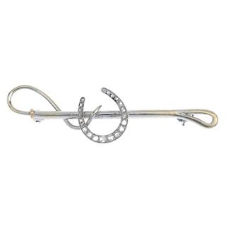 A diamond novelty brooch. Designed as a rose-cut diamond horseshoe, atop a riding crop. Length 5.4cm