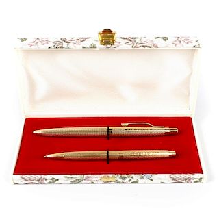 A 9ct gold ballpoint pen set. Comprising two examples each having engine turned bodies with personal