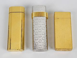 A selection of three lighters. Comprising two gold plated Cartier examples, both having ribbed textu