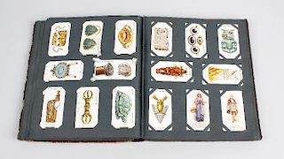A box containing a cigarette card album holding a mixed selection of assorted cigarette cards, plus