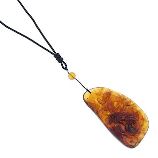 A carved Burmese amber dragon pendant. The black neck-cord suspending a carved tablet of Burmese amb