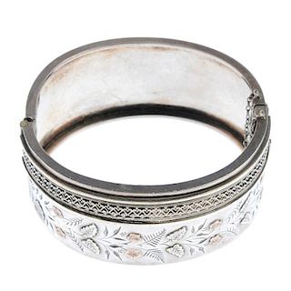 A late 19th century silver hinged bangle. With wire and beadwork border and applied leaf and flower