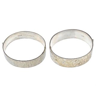 Three silver bangles. To include a hinged bangle, with scroll engraved decoration, a 1970s bark-effe
