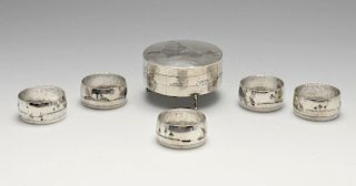 A white metal trinket box of circular form raised on three scroll feet, and five similar napkin ring