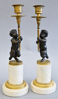 Pair of French Bronze and Marble Figural Candlesticks, having bronze putti with hoof feet holding gilt bronze candlesticks on white marble base, heigh