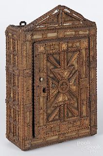 Tramp art carved hanging cabinet, 20th c., with an open carving, backed with fabric panels