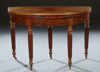 French Carved Walnut Demilune Games Table, 19th c., the lifting top with a central baize lined gaming surface, on turned tapered reeded legs on caster