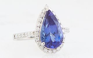 Lady's 18K White Gold Dinner Ring, with a 4.09 ct. pear shaped tanzanite atop a conforming border of tiny round diamonds, the shoulders of the band al