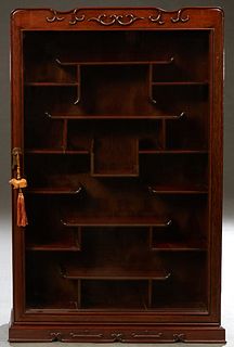 Chinese Carved Mahogany Hanging Etagere Wall Cabinet, 20th c., the serpentine top over a glazed door opening to an interior mounted with numerous shel