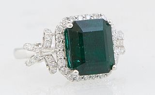 Lady's Platinum Dinner Ring, with a 6.08 carat emerald atop an octagonal border of small round diamonds, flanked by diamond mounted bow form lugs, tot