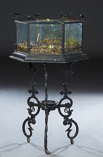 Cast Iron Terrarium, c. 1920, the hexagonal glass sided top on scrolled tripodal supports joined by a circular stretcher/shelf, H.- 46 in., W.-23 in.,