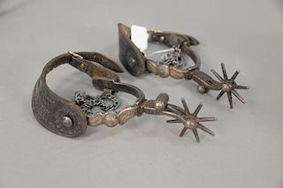 Pair of cast iron Western Cowboy spurs with silver inlay and tooled leather straps, eight pointed star rowels.