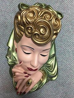 An Art Deco painted plaster figural mask, her golden hair partially covered by a green scarf, rings