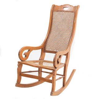 Mecedora. SXX. Elaborada en madera con respaldo y asiento de bejuco tejido. Decorada con roleos y molduras orgánicas.