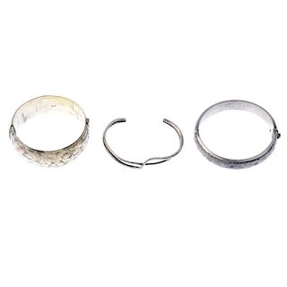 A selection of silver bangles. The first designed as a wide hinged silver bangle with foliate engrav